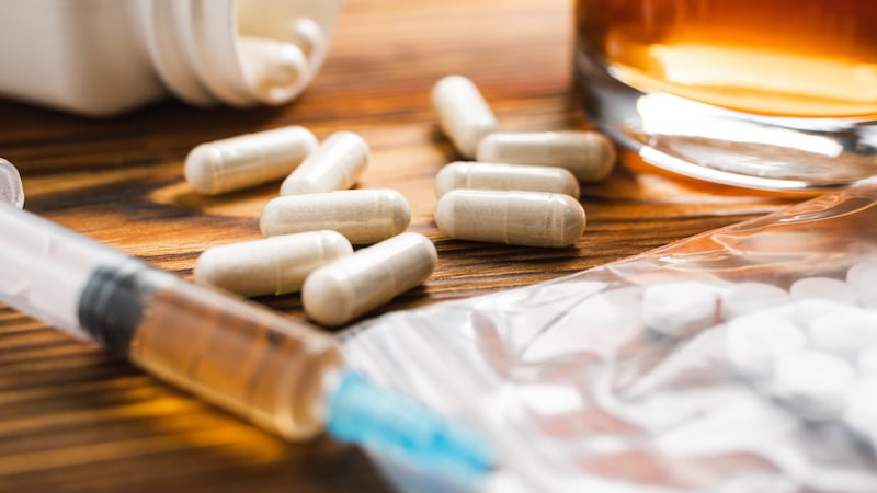 White pills, syringe with a drugs dose, narcotics, glass with alcohol drink on a wooden table,...