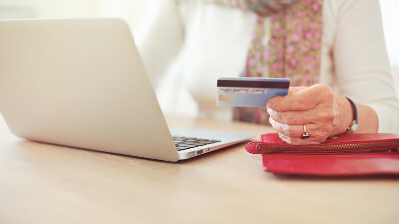 Senior woman's hand holding a credit card while in front of the laptop shopping online